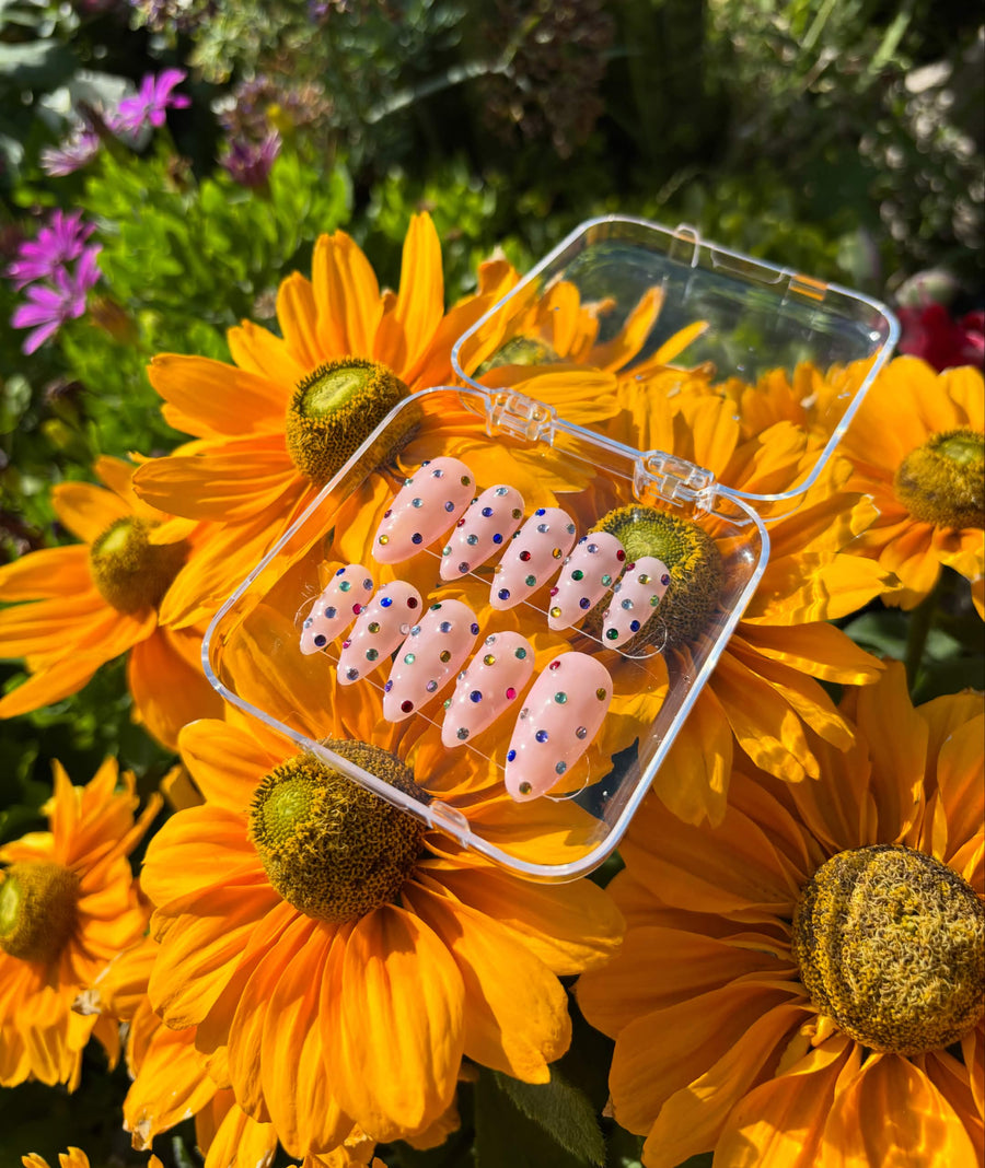 Confetti Kisses press-on nails — ten almond nails in milky peach, scattered with hand-set emerald, sapphire, ruby and gold rhinestones