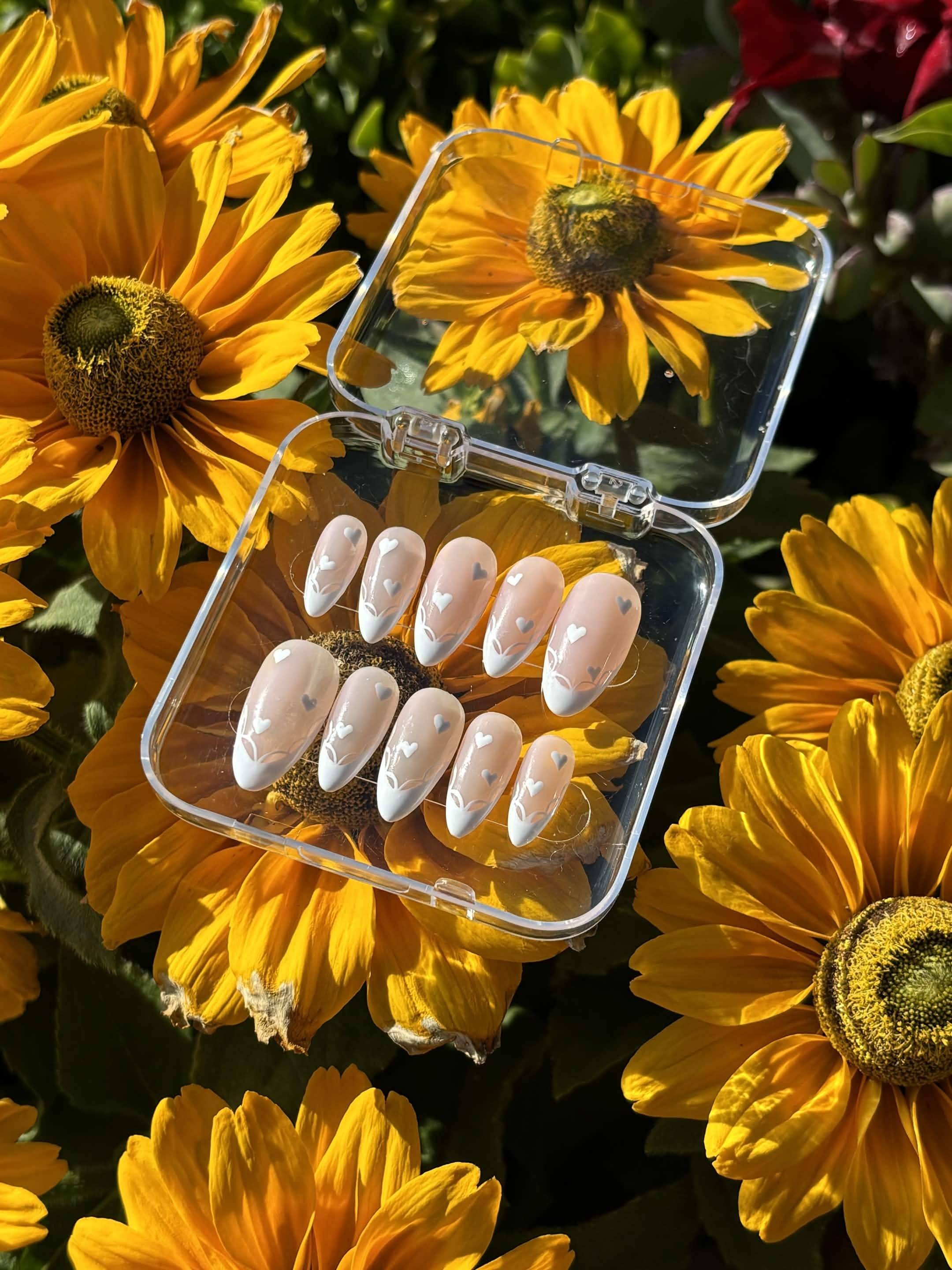 Blushing Hearts press-on nails — ten almond nails with white French tips, hand-painted hearts and fine white line-work on a milky nude base, in an open clear case