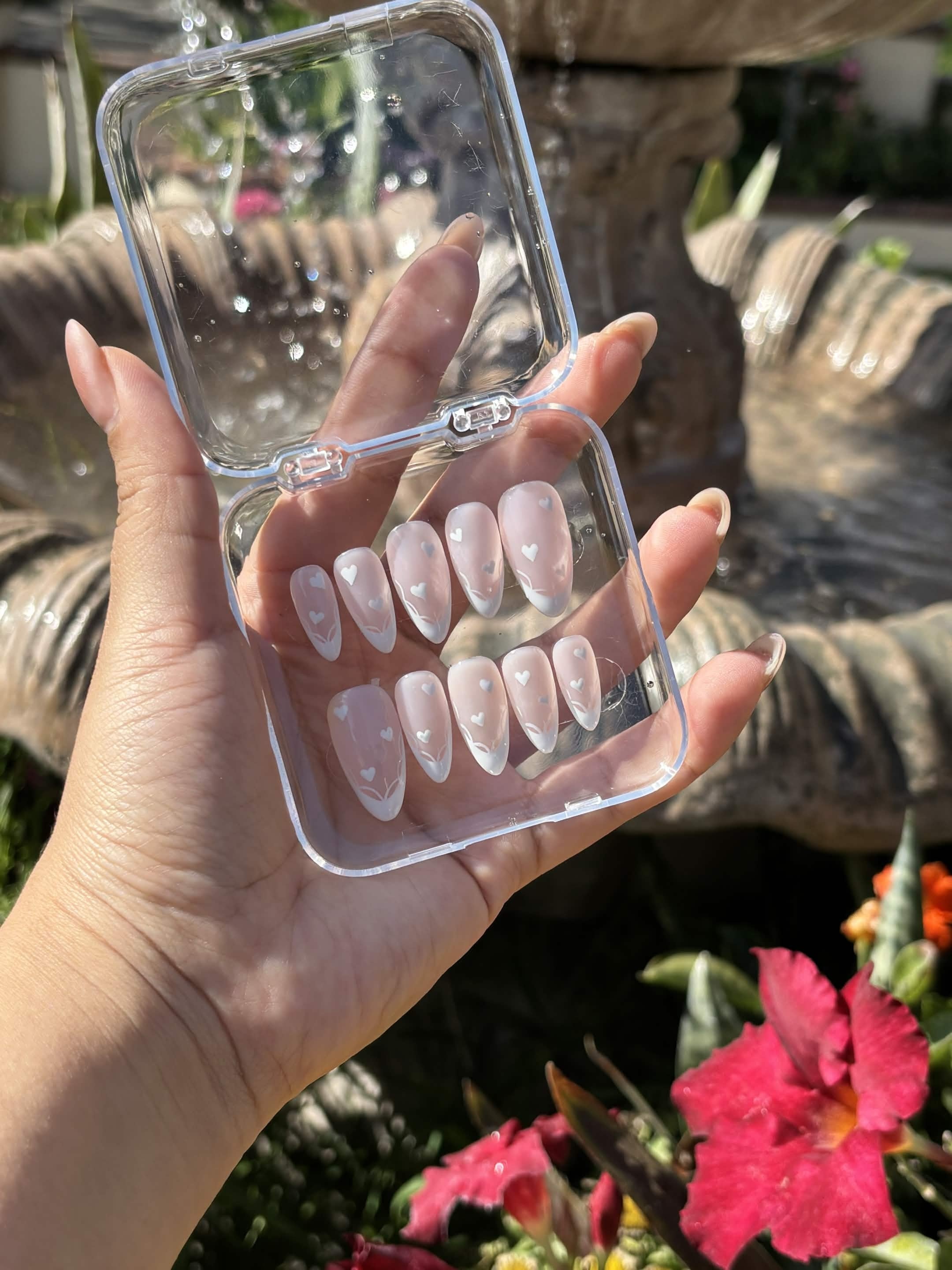 Blushing Hearts press-on nail set held in the hand, showing the sheer nude base and crisp white tips